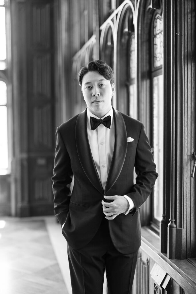 Groom in black tuxedo standing in Hempstead House interior before wedding.