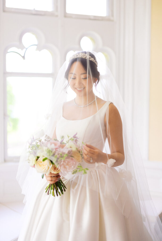 Bride holding bouquet in front of sunlit window at Hempstead House wedding.
