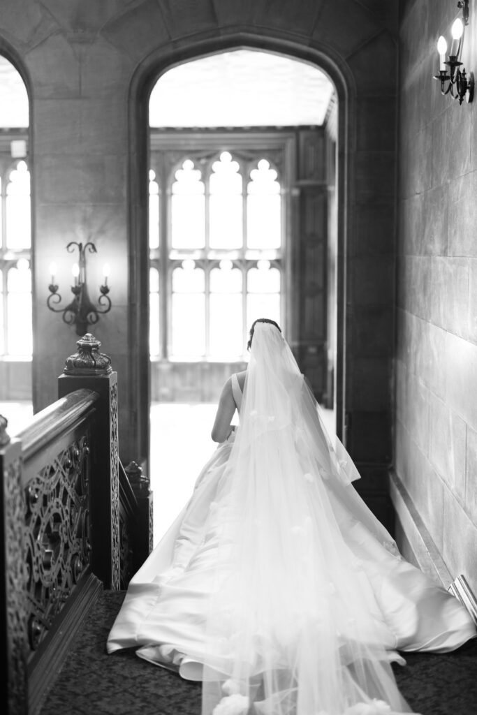 Bride descending staircase inside Hempstead House mansion on wedding day.