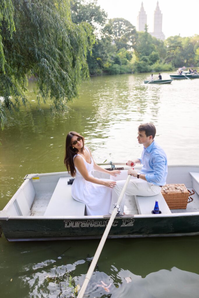 A couple during their NYC engagement session at the Central Park Boat House, sitting in a rowboat and sharing a romantic moment on the lake.