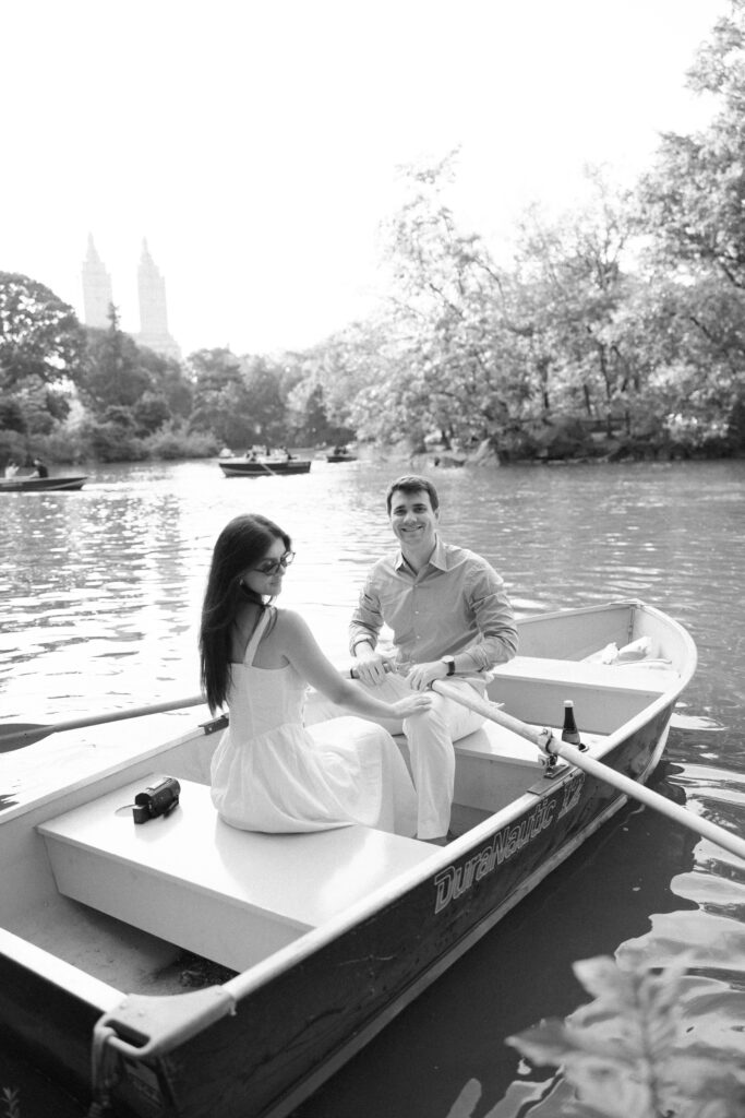 A couple during their NYC engagement session at the Central Park Boat House, sitting in a rowboat and sharing a romantic moment on the lake.
