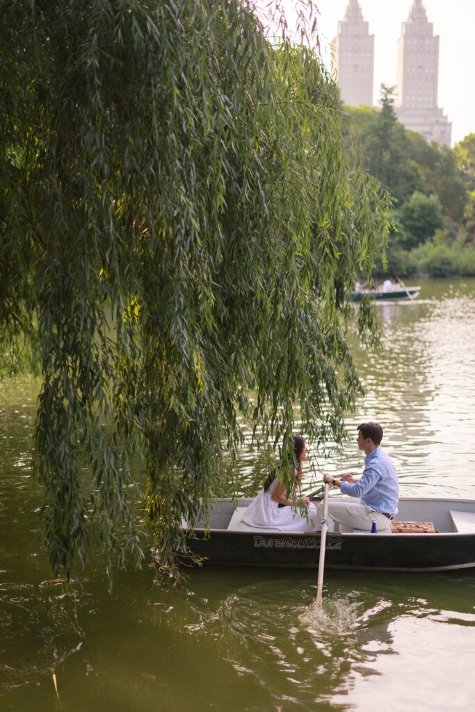A couple during their NYC engagement session at the Central Park Boat House, sitting in a rowboat and sharing a romantic moment on the lake.