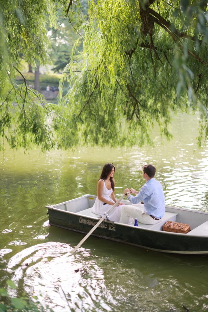 A couple during their NYC engagement session at the Central Park Boat House, sitting in a rowboat and sharing a romantic moment on the lake.