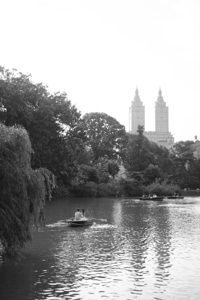 A couple during their NYC engagement session at the Central Park Boat House, sitting in a rowboat and sharing a romantic moment on the lake.