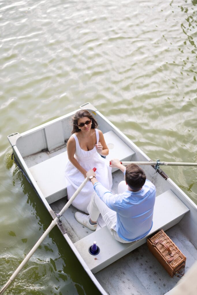 A couple during their NYC engagement session at the Central Park Boat House, sitting in a rowboat and sharing a romantic moment on the lake.