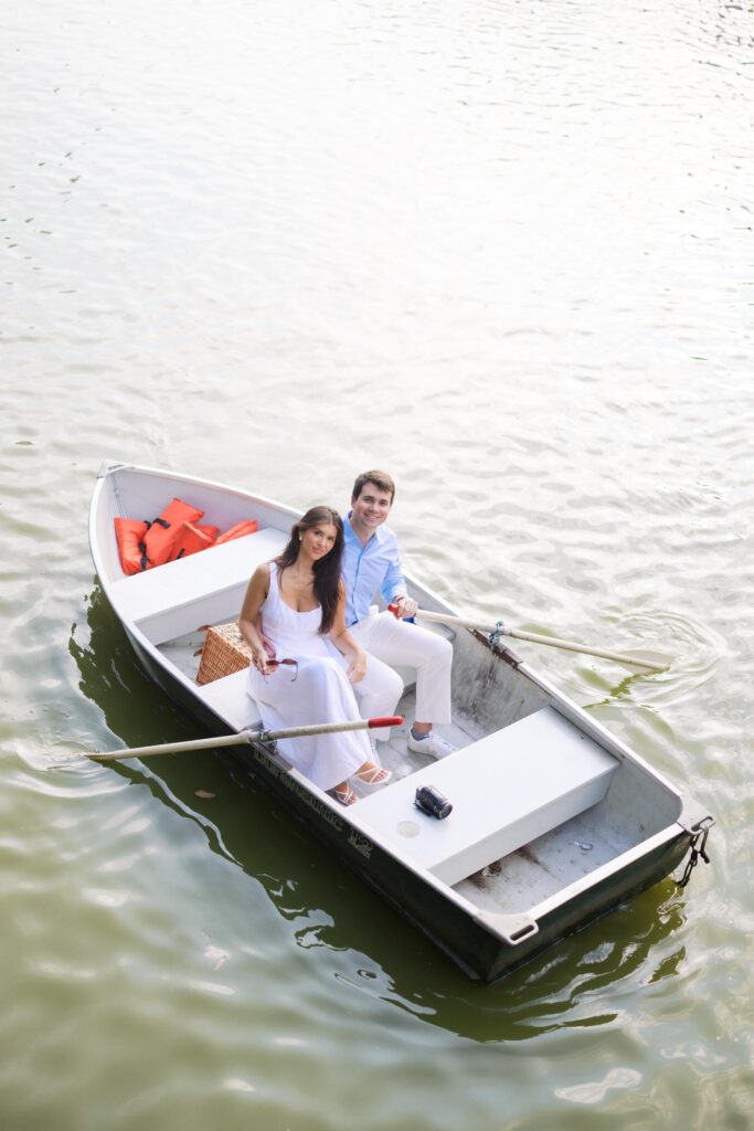 A couple during their NYC engagement session at the Central Park Boat House, sitting in a rowboat and sharing a romantic moment on the lake.