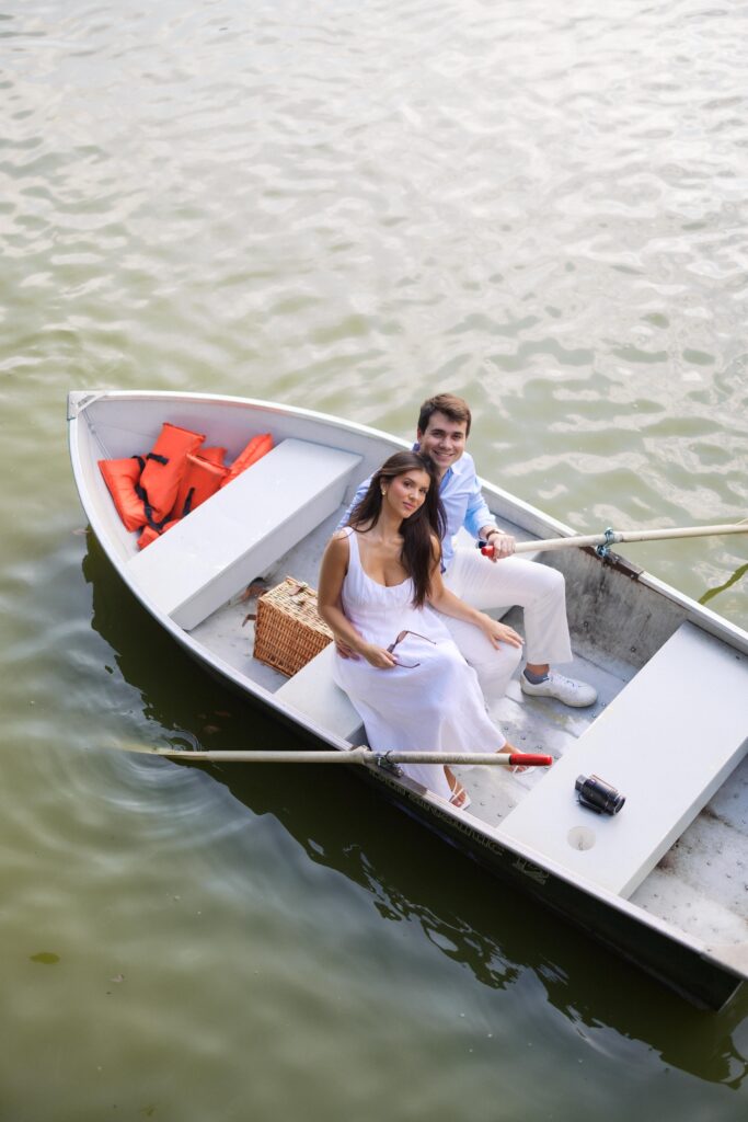 A couple during their NYC engagement session at the Central Park Boat House, sitting in a rowboat and sharing a romantic moment on the lake.